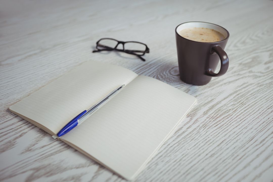 Open notebook with a cup of tea on a wooden surface